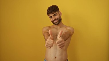 Yakışıklı, sakallı genç bir adam izole edilmiş sarı arka plan için başparmak kaldırıyor.