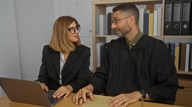 Kadın ve erkek bir ofis ortamında birlikte çalışıyor, yargıç gibi giyinmiş bir adamla ve avukat gibi giyinmiş bir kadınla, hukuki konuları tartışıyorlar..