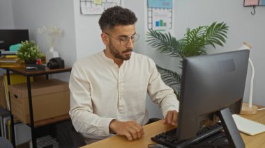 Ofiste çalışan genç bir İspanyol, modern kapalı bir çalışma alanında bilgisayarda daktilo yazıyor..