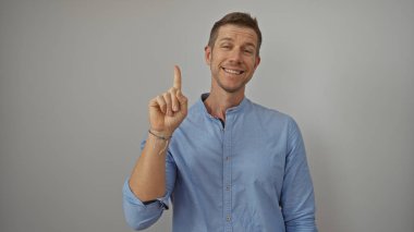 Genç adam özgüvenle gülümserken, beyaz bir arkaplanı işaret ederek, üstünkörü mavi bir gömlek giyerek pozitifliğini ve fikirlerini aktarıyor..