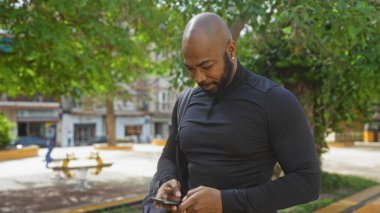 Şehir parkında akıllı telefon kullanan yakışıklı bir zenci.