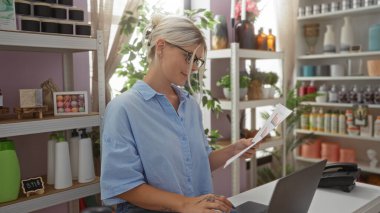 Ev dekorasyonu mağazasında çalışan bir kadın, dizüstü bilgisayarın başında duran ve çeşitli dekoratif eşyalarla çevrelenmiş bir halde profesyonel ve düzenli bir ortam gösteren evrakları inceliyor..