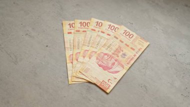 Meksika 100 pezoluk banknotlar gri beton bir yüzeye saçılmış, her notada renkli tasarım ve tarihi figür sergileniyor..