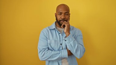 Kel kafalı ve sakallı yakışıklı Afro-Amerikalı adam izole edilmiş sarı arka plan duvarına nazikçe poz veriyor.