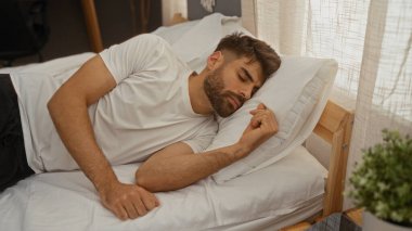 Genç adam rahat bir yatak odasında uyuyor, doğal ışıklandırmayla, beyaz bir gömlek giyiyor, huzurlu, rahat ve dinleniyor, sakallı ve yakışıklı..