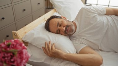 Orta yaşlı, İspanyol bir adam evdeki rahat bir yatak odasında huzur içinde uyuyor. Evde huzurlu ve rahatlatıcı bir anı yakalıyor..