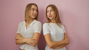 Sarışın ikiz kardeşler pembe bir arka plana karşı kollarını kavuşturup aile sevgisi ve bağlarını gösteriyorlar..