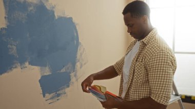 Yeni bir oturma odasının içinde boyanmış renkleri seçen bir adam, projeyi yeniden dekore etmek için mavi duvar örnekleriyle tasarım tasarlıyor..