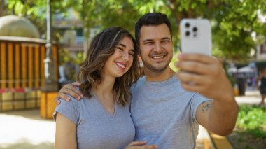 Güneşli şehir parkında selfie çeken çift ilişkilerinde sevgi ve mutluluk gösteriyor.
