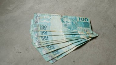 Brezilya 100 reais banknotları somut bir yüzey üzerinde sergileniyor. Brezilya 'daki finansal temalar ve para birimlerine ayrıntılı portreler ve karmaşık tasarımlarla örnek veriliyor..