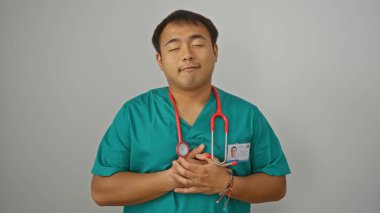 Genç Çinli bir adam steteskopla tıbbi önlük giyiyor, izole edilmiş beyaz bir arka planın başında duruyor..