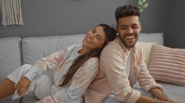 Çift modern oturma odalarında rahat bir kanepede birlikte gülümsüyor.