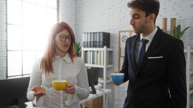 İş ortakları, bir erkek ve bir kadın, modern ofis ortamında kahve fincanları tutarken sohbet ediyorlar, içeride işbirliği ve takım çalışması sergiliyorlar, profesyonel etkileşimleri vurguluyorlar..