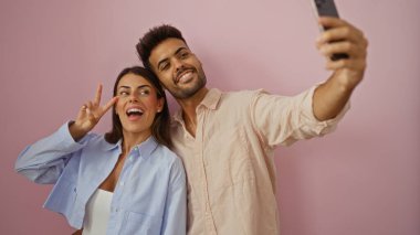 Gülümseyen adam ve kadın pembe arka planda selfie çekiyorlar. Aşkı ve ilişkiyi gösteriyor.