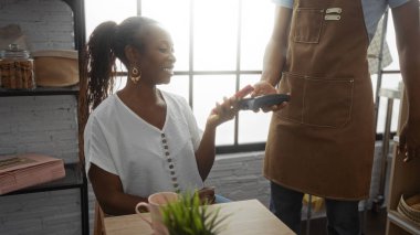 Kadın gülümserken, iskambil okuyucusuyla birlikte pastanenin iç kısımlarında, penceresinden süzülen mal ve güneş ışığıyla gülümsüyor.