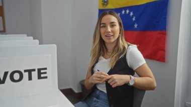 Genç, çekici, sarışın bir kadın, Venezuela 'daki bir seçim kolejinde oy kullanırken, arka planda belirgin bir Venezuela bayrağı sergileniyor..