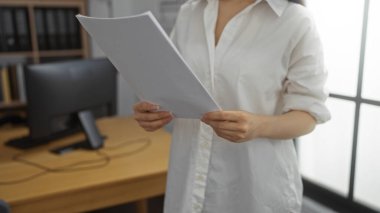 Ofis içi bir ofiste elinde kağıtlar olan genç bir kadın, arka planda bir bilgisayarla profesyonel bir iş ortamı ve iş ortamı öneriyor..