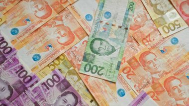 Düz bir yüzeye dağılmış 20, 50, 100 ve 200 peso değerinde Filipin banknotları çeşitli kahramanlar ve tarihi semboller sergiliyor..