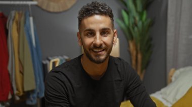 Evdeki yatak odasında oturan yakışıklı, genç İspanyol bir adam, dostça bir gülümsemeyle yatakta oturuyor..