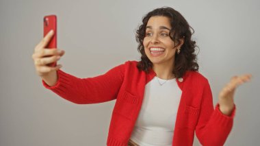 Kırmızı kazaklı genç bir İspanyol kadın izole edilmiş beyaz bir arkaplan üzerinden görüntülü bir telefon görüşmesi yapıyor..