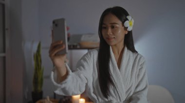 Kaplıcada selfie çeken beyaz cüppeli, saçlı, çiçekli bir kadın.