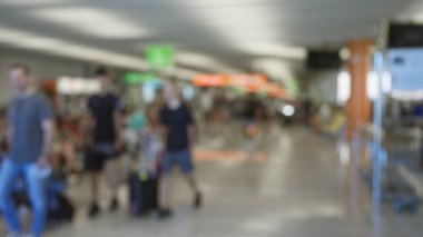 Blurred travelers walking in airport terminal with defocused background showing bokeh lights and out of focus signs clipart