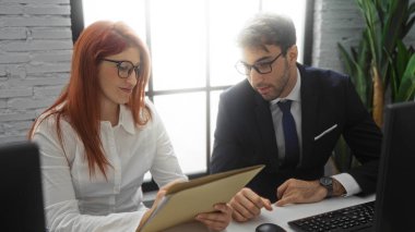 İspanyol iş adamları, bir erkek ve bir kadın, modern ofis ortamında bir proje üzerinde işbirliği yapıyor, takım çalışmasını, profesyonelliği ve kapalı alandaki kurumsal ortaklığı ön plana çıkarıyor..