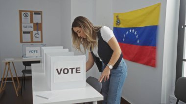 Genç, çekici, sarışın bir kadın, Venezuela 'da kapalı bir seçim salonunda arka planda Venezuela bayrağıyla oy veriyor..