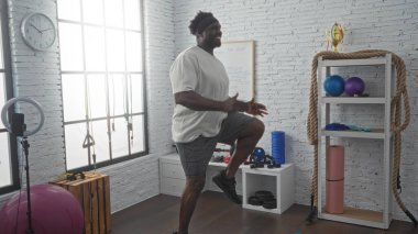 Yakışıklı, Afro-Amerikan bir adam spor salonunda spor yapıyor. Spor aletleri ve spor aletleri ile çevrelenmiş, fiziksel kondisyonuna olan bağlılığını vurguluyor..