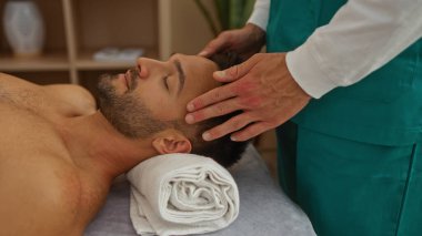 Bir sağlık merkezindeki masörden havlu ve iç dekorasyonla kafa masajı alan bir adam.