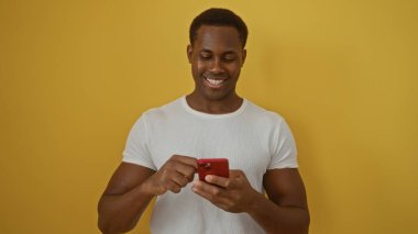 Genç adam, telefonu parlak sarı arka planda kullanırken gülümsüyor ve modern bir atmosfer yaratıyor..