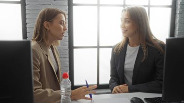 Modern bir ofis ortamında, ortaklık ve strateji üzerine odaklanmış işbirliği ve profesyonel çalışma ortamı sergileyen iki sarışın iş kadını.