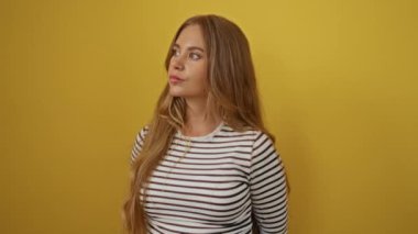 Ciddi yüzlü, çizgili tişört giyen, sarışın, doğal ve sade görünen, izole edilmiş sarı arka planı olan, kamera önünde resmi bir ifadeyle yakalanan genç bir kadın.