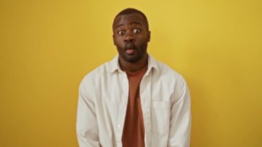 Sarı arkaplan önünde dikilen Afro-Amerikalı adam dudaklarını kullanarak komik ve komik hareketlerle komik bir balık suratı yapıyor.