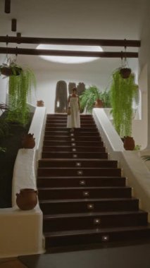 Beyaz elbiseli genç İspanyol kadın, Lanzarote, kanarya adalarında asılı bitkiler ve çömlek dekoru olan bir köy müzesi olan del campesino müzesinin merdivenlerinden iniyor.