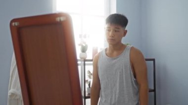 Çapraz kollu genç adam, sakin bir spa odasında duruyor, yansıtıcı bir tavır sergiliyor, hafif ışıklandırma ve minimalist dekorla çevrili, refah ve rahatlığı vurguluyor..