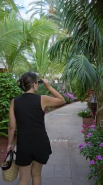 Lanzarote 'deki tropikal bitkilerle çevrili yemyeşil yolda yürüyen bir kadın, sepet taşıyan kanarya adaları.