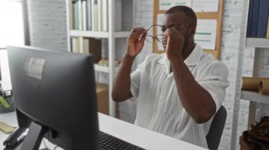 Ofis ortamında gözlük takan genç adam etrafı kitaplık ve belgelerle çevrili bir bilgisayarda çalışıyor..