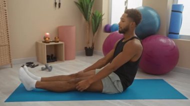 Spor salonunda spor aletleri ve yoga minderiyle egzersiz yapan genç adam.