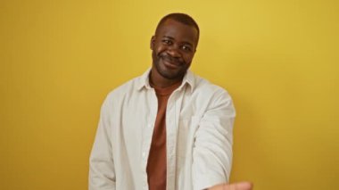 Gömleği açık duran Afro-Amerikan bir adam. Avuç içi yardım ve izole edilmiş sarı arka plan üzerinde kabullenme teklif ediyor.