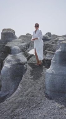 Lanzarote kanarya adalarında volkanik arazide yürüyen bir kadın. Güneş gözlüklü beyaz bir elbise giyiyor.