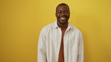 Afro-Amerikalı bir adam ayakta dikilip göz kırpıyor, mutlu ve neşeli bir ifade izole edilmiş sarı bir arka planda, kameraya seksi ve kendinden emin bakıyor.