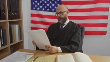Erkek yargıç, arka planda Amerikan bayrağı olan belgeleri okuyor.