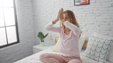 Genç bir kadın yatak odasında, yatak odasında, gözleri kapalı ve rahat bir şekilde, yastıklarla ve bitkilerle çevrili bir şekilde meditasyon yapıyor.