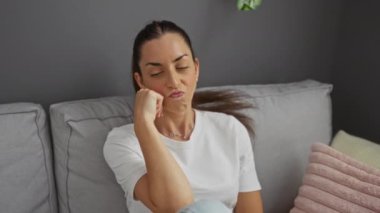 Kanepede dinlenen, düşünceli ve düşünceli görünen, sakin iç mekan ortamını ve atmosferi geliştirmek için günlük kıyafetlerini sergileyen bir kadın..