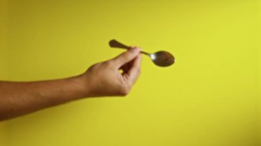 Bir kaşığı canlı sarı arka planda tutan, günlük nesnelere odaklanarak basitlik ve minimalizm gösteren bir el.