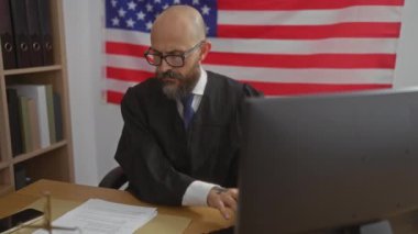 Yargıç, arka planında Amerikan bayrağı olan bir ofiste masasında çalışıyor.