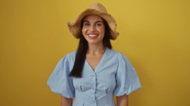 Sarı arka planda sırıtan İspanyol kadın. Hasır şapka ve açık mavi elbise giyiyor.