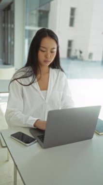 Parlak ofis ortamında dizüstü bilgisayarına odaklanan bir kadın profesyonel ve konsantre bir atmosferi ön plana çıkarıyor..