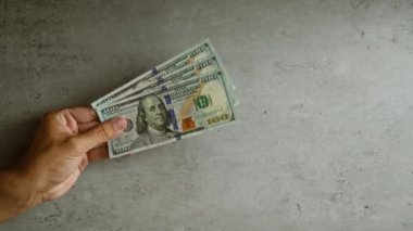 Elele tutuşan Amerikan doları banknotları somut bir arka plana karşı, para ve zenginliği vurguluyor